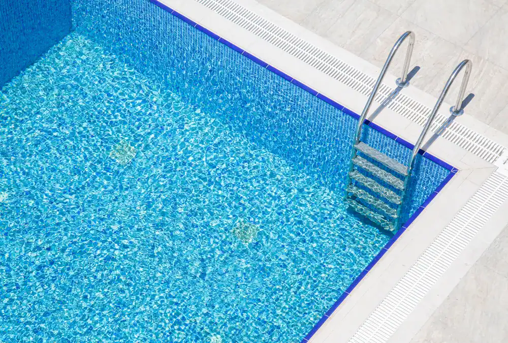 A clean, empty swimming pool with clear blue water and a metal ladder at the corner, surrounded by a white tiled deck—showcasing expert pool construction in Douglas County, GA.
