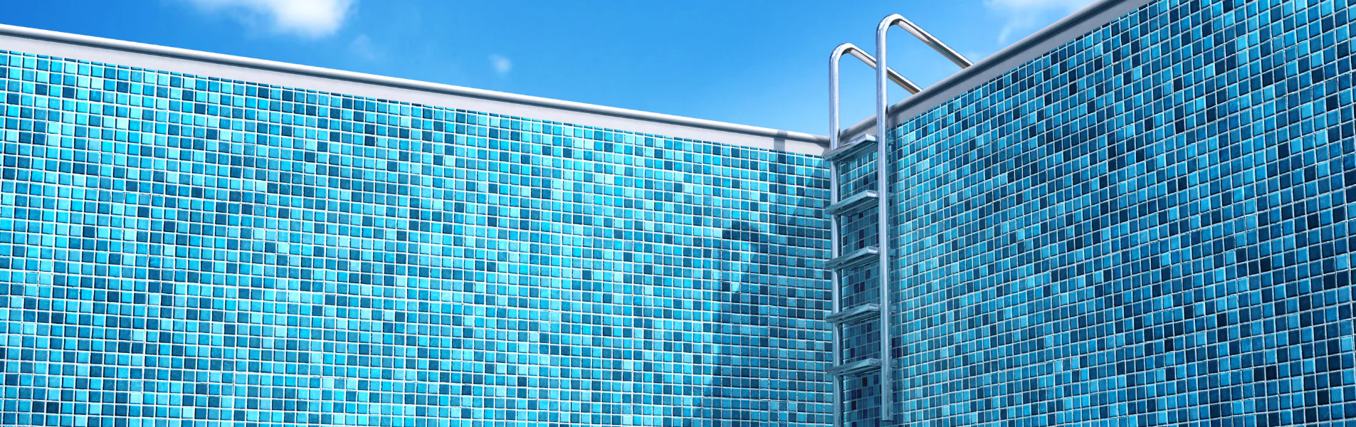 A close-up of the corner of a modern swimming pool with blue mosaic tiles and a metal pool ladder against a clear blue sky.