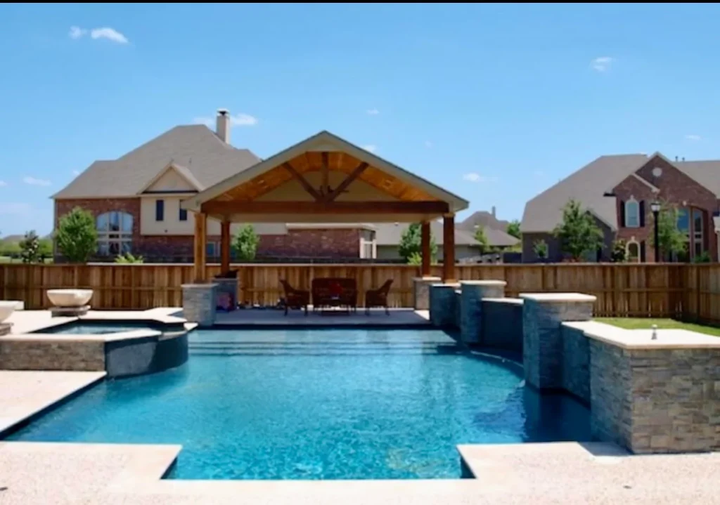 Modern backyard pool features stone accents, a hot tub, and covered patio in a quiet suburban neighborhood.