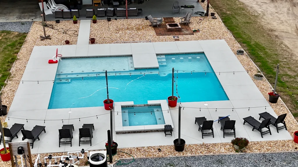 A backyard pool with a hot tub, lounge chairs, string lights, and potted plants creates an inviting oasis.