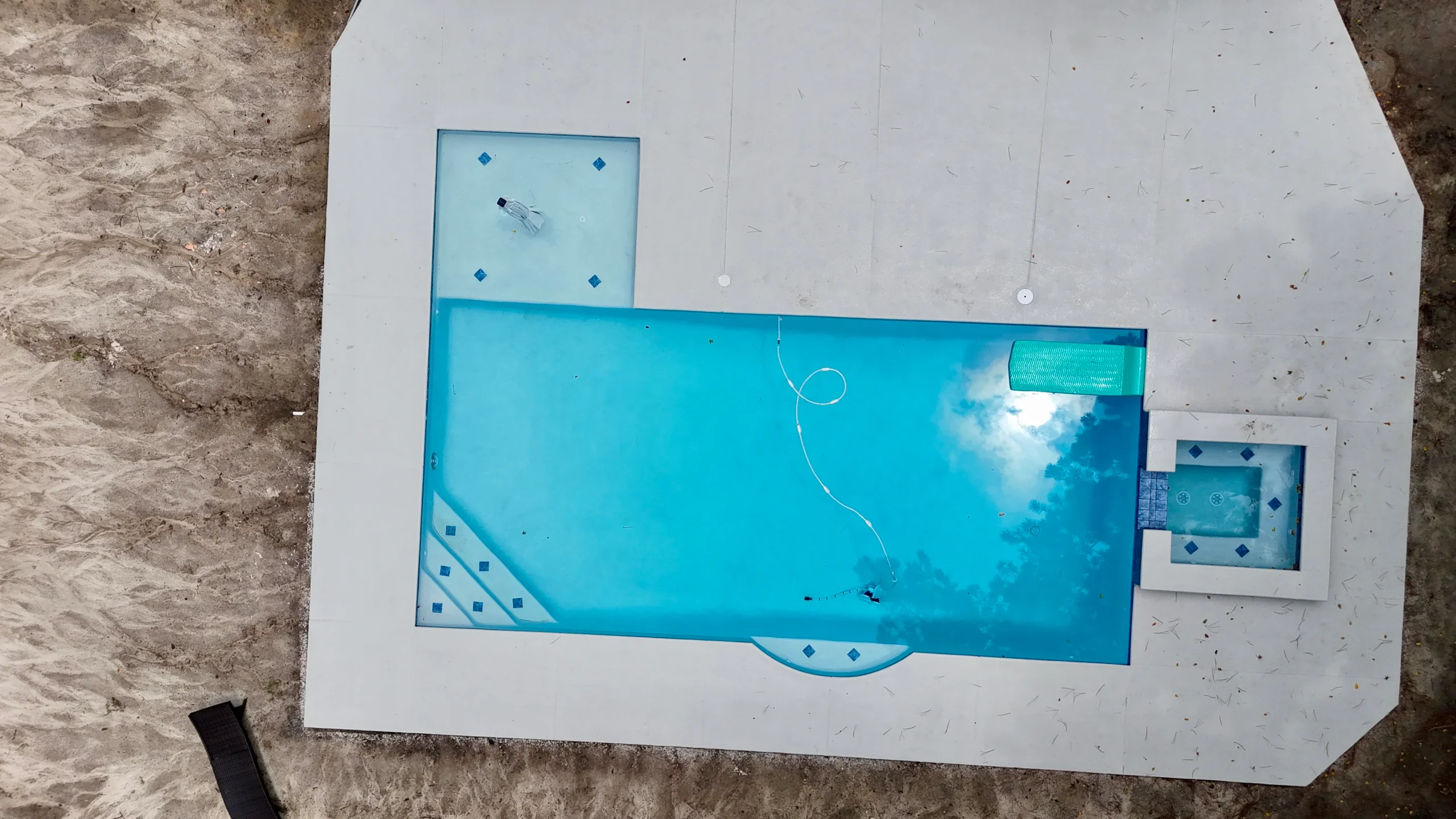 A rectangular swimming pool with a small attached spa is surrounded by concrete, viewed from above.